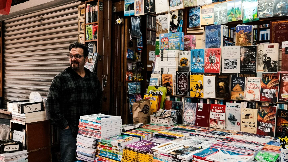 Smiling bookseller standing among stacks of books at a street bookstore