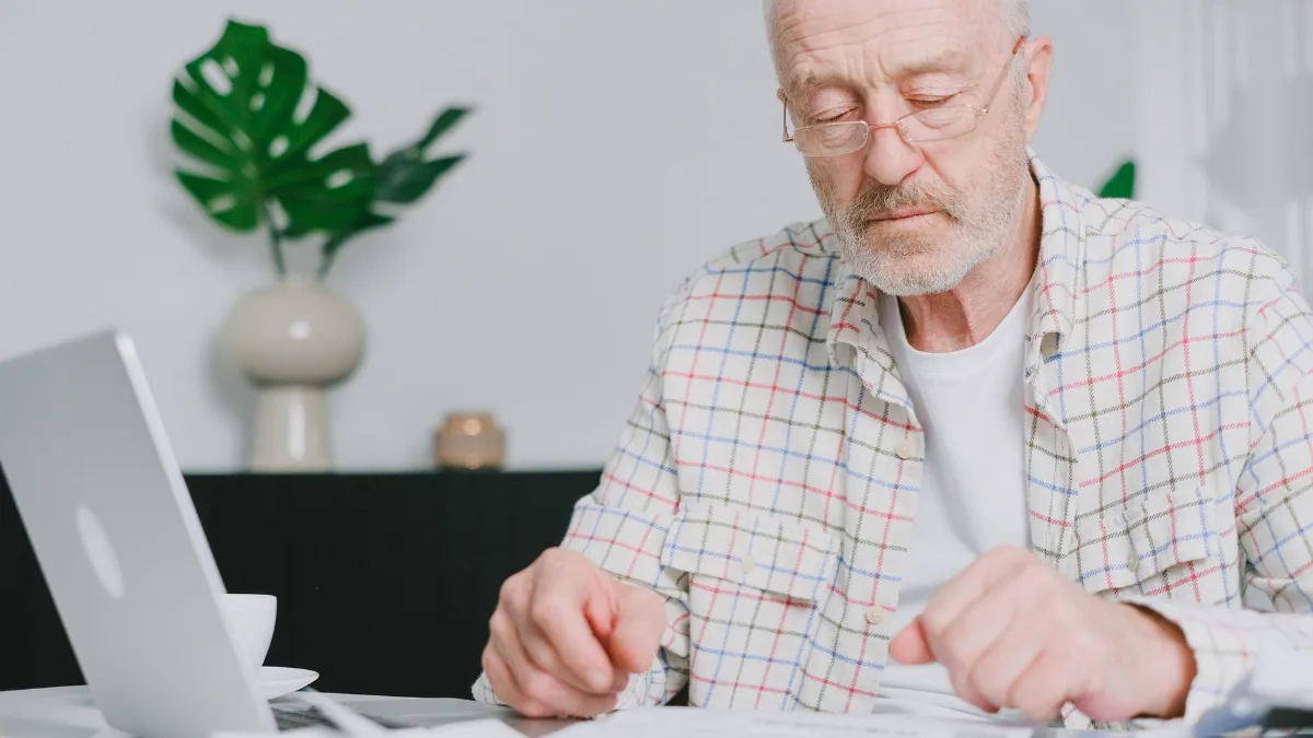 Older man reviewing paperwork at his desk next to a laptop