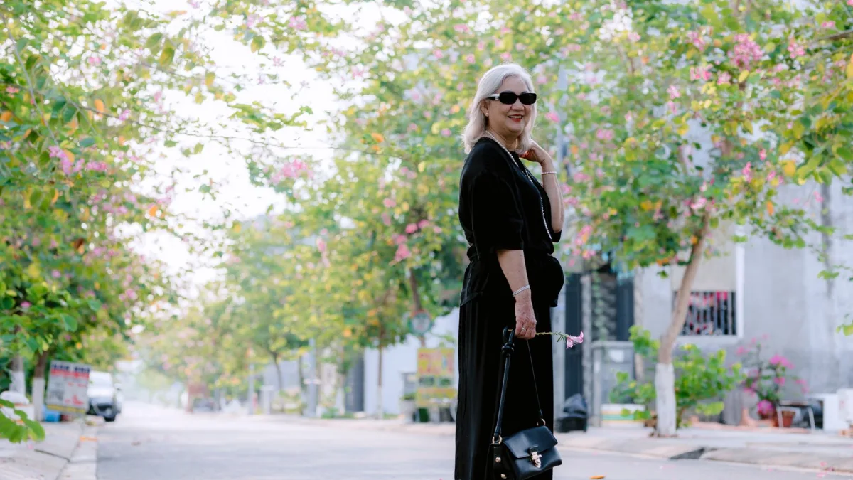Stylish older woman in sunglasses walking down a tree-lined street